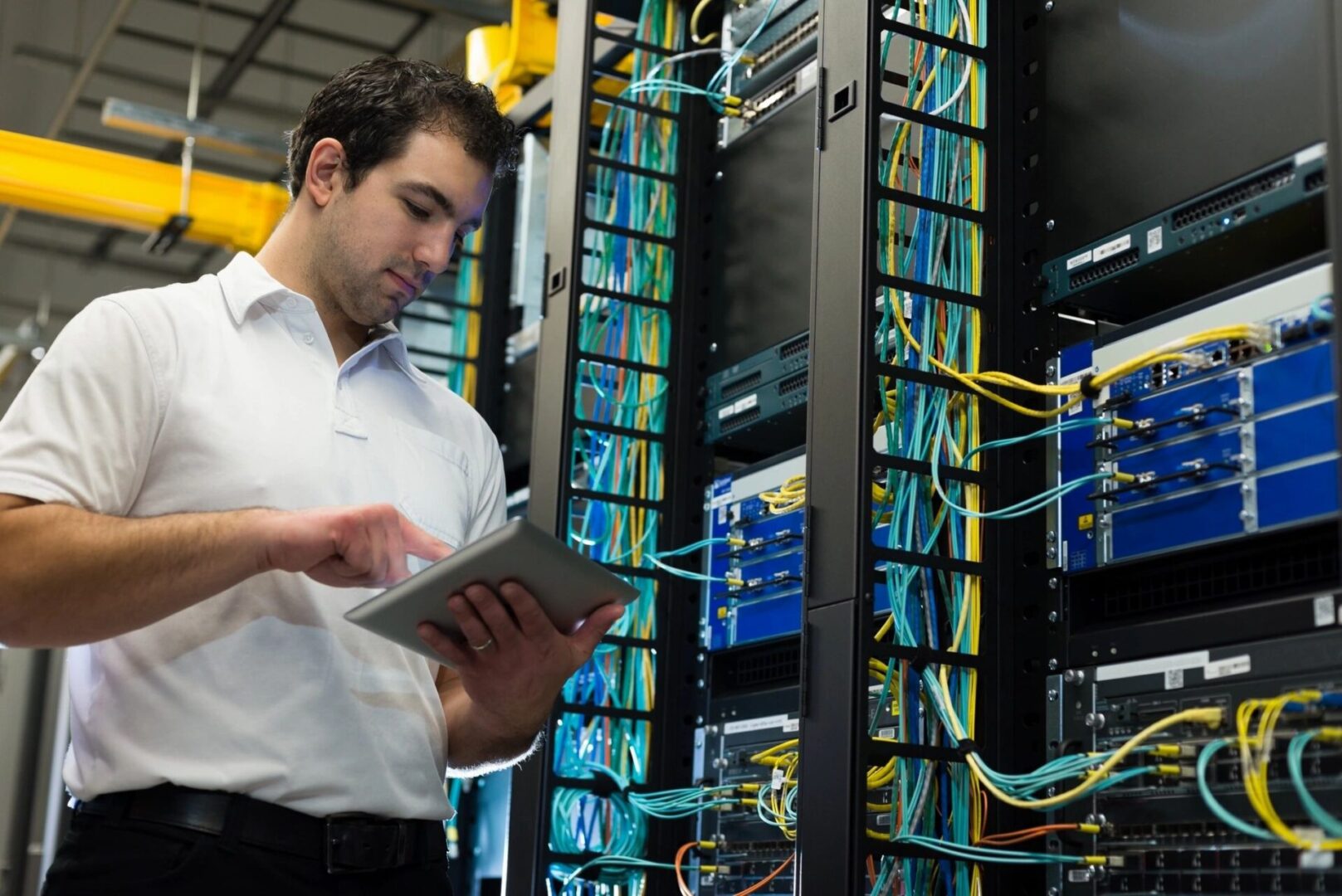 A man holding a tablet in front of server racks.