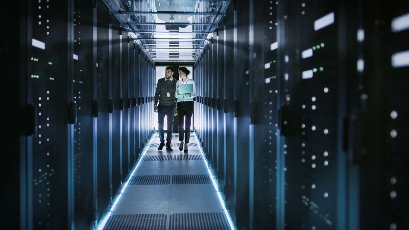Two people are walking through a hallway of servers.